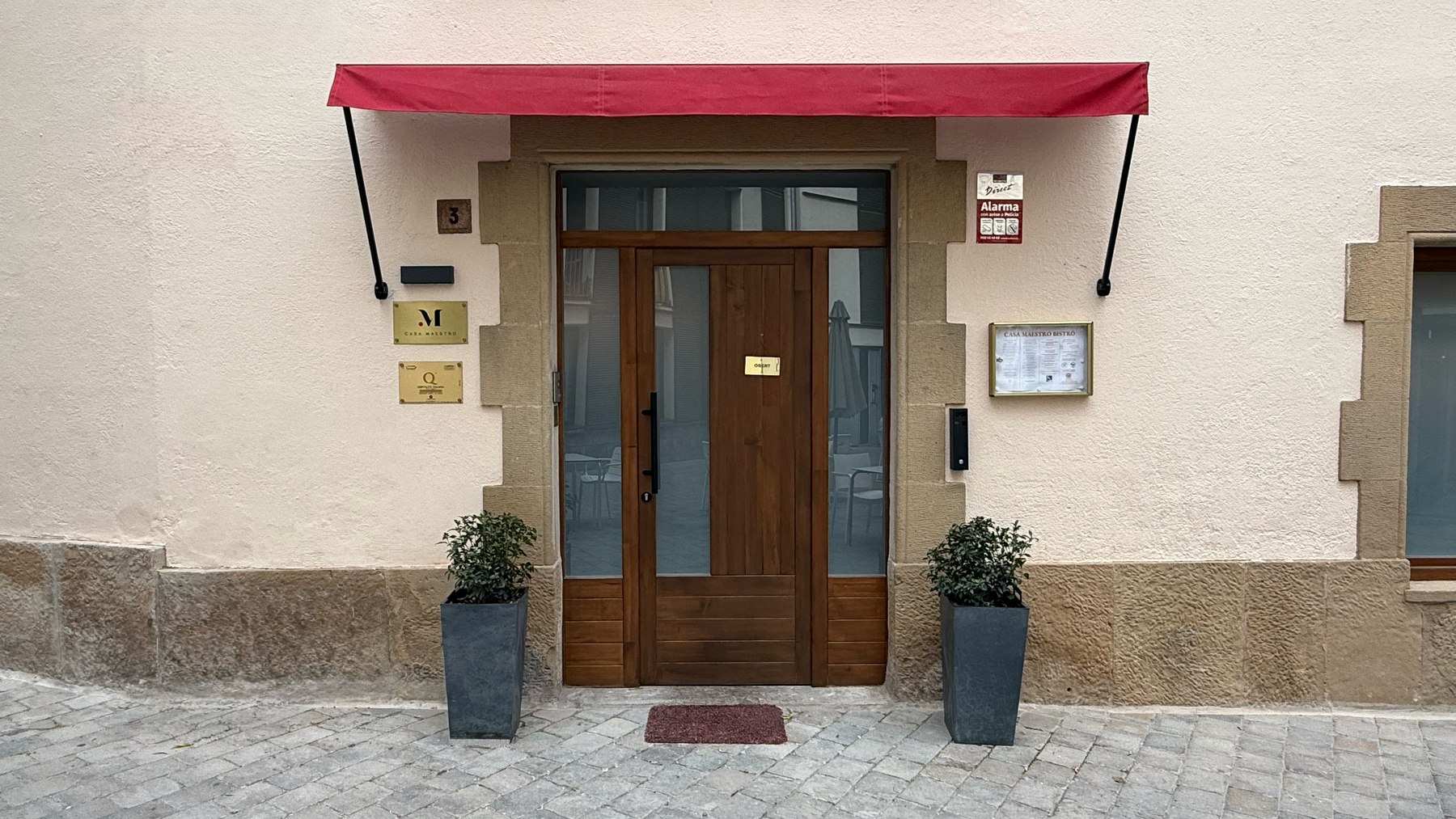 Entrada de Casa Maestro Bistró con fachada de piedra y toldo rojo en Castellterçol
