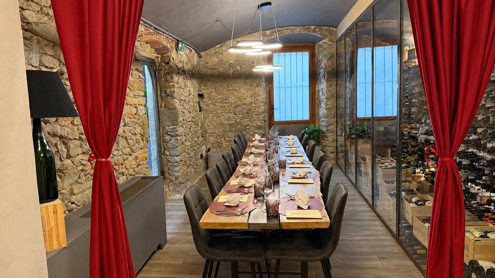 Sala privada de Casa Maestro con mesa larga montada, cortinas rojas, muros de piedra y bodega acristalada